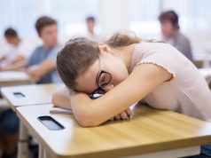 Tired bored teenage school girl sleeping at desk in classroom