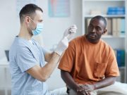 Overall Risk of Myopericarditis Low After COVID-19 Vaccine Side view portrait of male nurse drawing medicine into syringe while vaccinating African-American man in clinic or hospital